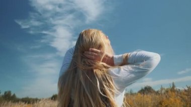 Güzel elbiseli genç bir kız saçlarını güçlü bir rüzgarda savuracak. Tarlada bir kız.