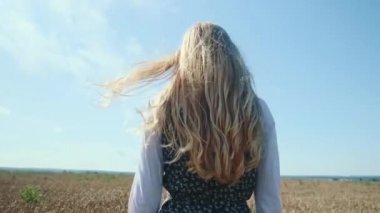 Güzel elbiseli genç bir kız dikenli kazık ve buğdayla bir tarlada yürüyor..