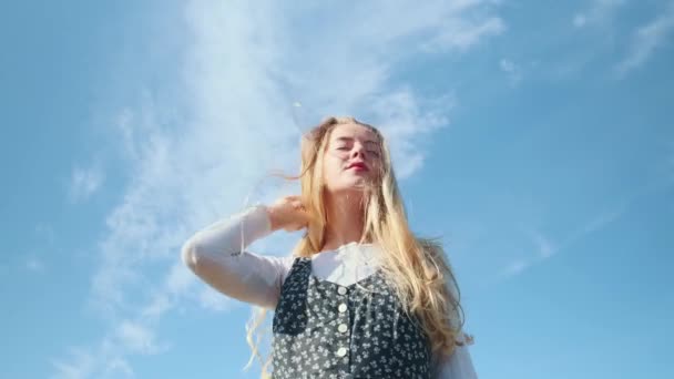Een jong meisje in een prachtige jurk tegen de blauwe lucht. Een mooi meisje poseert voor de camera. — Stockvideo
