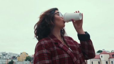 Gözlüklü genç bir kız kahve içer ve cep telefonuna bakar..