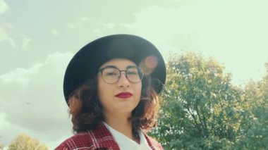 Kafkas görünümlü, gözlüklü ve güneşli havada parkta yürüyen mutlu bir kız. Yakın plan.