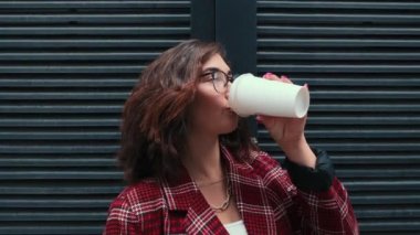 Genç bir kız temiz havada kahve içiyor. Mutlu bir kız iş merkezinin yakınında kahve içiyor..