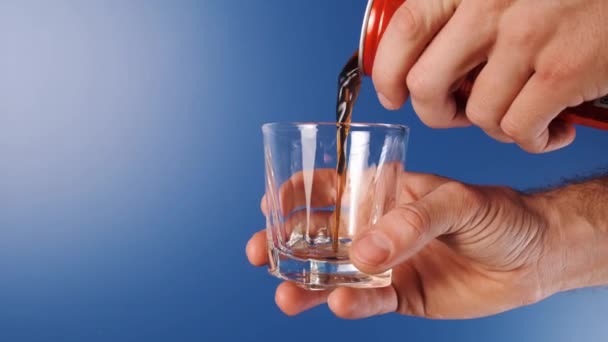 Het middelste frame is een slow-motion shot van een hand die een blik Cola vasthoudt en in een glas op een blauwe achtergrond giet.. — Stockvideo
