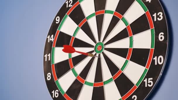 Een spelletje darts. Hij gooit pijlen naar het doelwit. En iemand gooit darts op een dartbord. Een dartbord hangend op een blauwe achtergrond. — Stockvideo