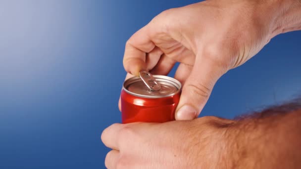 Close-up de um homem mão abrindo uma lata de refrigerante vermelho em um fundo azul em câmera lenta. Uma lata de Cola vermelha abre. — Vídeo de Stock