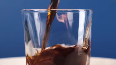 Mavi arka planda bir bardağa kola dökmek. Statik çerçeve. 4k görüntü.