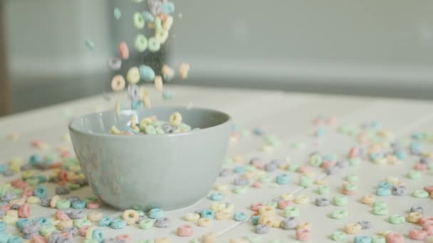 Les céréales de petit déjeuner sous la forme d'anneaux de maïs colorés tombent et remplissent le bol sur la table. Nourriture en gros plan sur fond de flocons épars. Flocons de maïs colorés et — Video