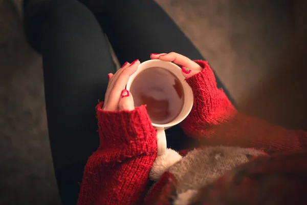 Top down shot of a Girl with a warming tea drink in hands sitting on the sofa with christmas colored fingernails and reindeer sweater. — Stock Photo, Image