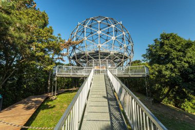Balaton Gölü, ormanlık tepeler ve uzak kıyı şeridine bakan Balatonboglar 'daki Xantos bakış açısındaki geometrik metal gözlem kubbesi, panoramik manzaralı, temiz tasarım ve parlak yaz atmosferine sahip modern bir manzara yapısı yaratıyor..