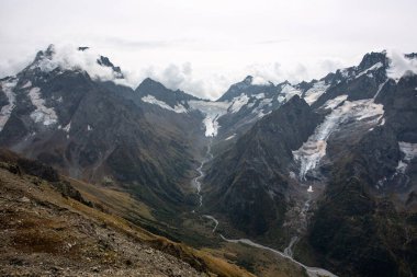 Bulutlarda kar tepeli dağ sıraları. Dağlık deresi olan bir vadi. Kafkaslar, Rusya