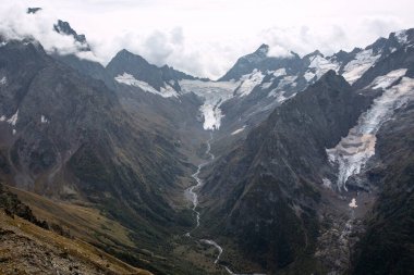 Bulutlarda kar tepeli dağ sıraları. Dağlık deresi olan bir vadi. Kafkaslar, Rusya