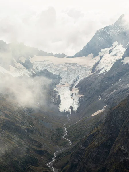 Snow capped mountain range in the clouds. Valley with a mountain stream. Caucasus, Russia — Stock Photo, Image