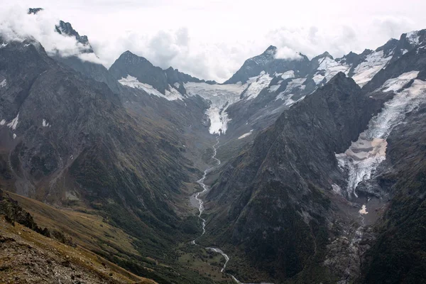 Bulutlarda kar tepeli dağ sıraları. Dağlık deresi olan bir vadi. Kafkaslar, Rusya