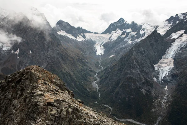 Gama de montanhas cobertas de neve nas nuvens. Vale com um riacho de montanha. Cáucaso, Rússia — Fotografia de Stock