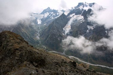 Bulutlarda kar tepeli dağ sıraları. Dağlık deresi olan bir vadi. Kafkaslar, Rusya
