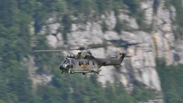 Hélicoptère militaire en vol à grande vitesse dans une vallée alpine verdoyante et rocheuse — Video