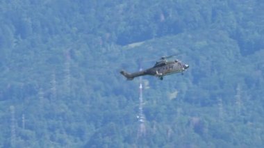 Askeri helikopter arka planda bir ormanla havada duruyor.