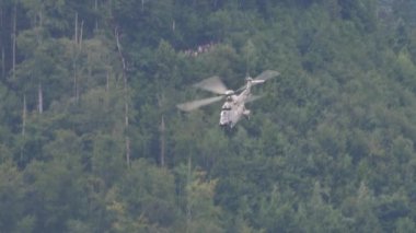Askeri helikopter maksimum hızda uçuyor ve arka planda ormanla kamufle oluyor.