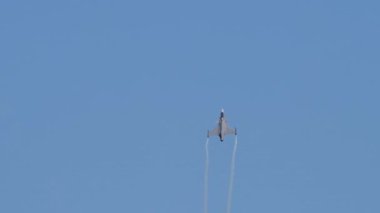 Savaşçı Jet, mavi gökyüzünde uçuyor, beyaz patikaları var.