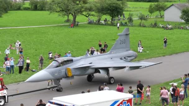 Luchtshow toeschouwers kijken naar een grijze militaire jet vliegtuig wordt getrokken door een tractor — Stockvideo