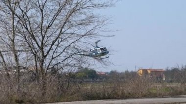 Polis helikopteri Agusta Bell AB-212 ağaçların arkasında uçuyor ve iniyor.