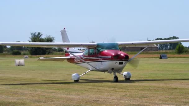 Małe prywatne lekkie samoloty w czerwono-białej liberii kołowania na trawiastym lotnisku — Wideo stockowe
