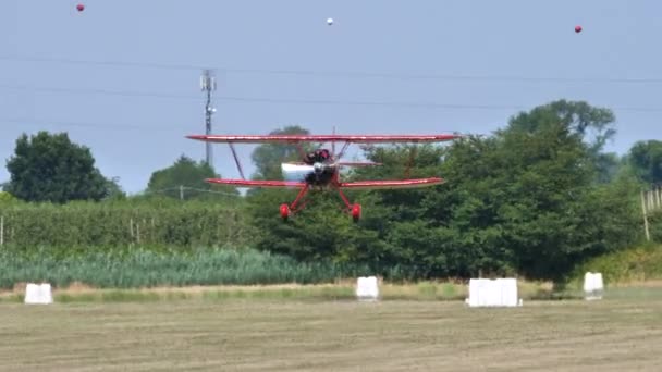 Retro biplano rojo aterrizando en una pista de aterrizaje de hierba en el campo en un día de verano — Vídeos de Stock