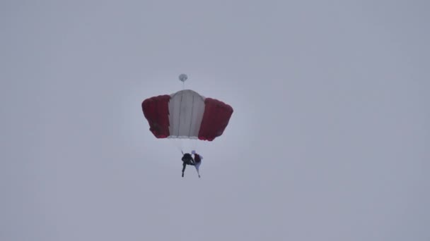 Fallschirmspringer öffnet eine rot-weiße Flagge, als er an einem sehr bewölkten Tag zwischen den Landebahnen landet — Stockvideo