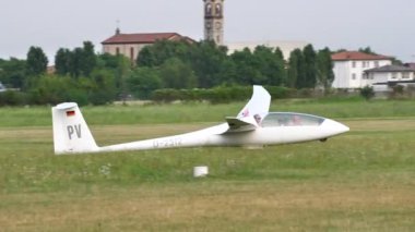Planör çimen pistine indikten sonra yavaşlar ve durur ve arka planda bir kilise vardır.