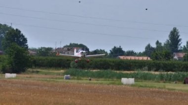 Ultralight beyaz uçağı küçük bir havaalanının çim pistinden kalkıyor.