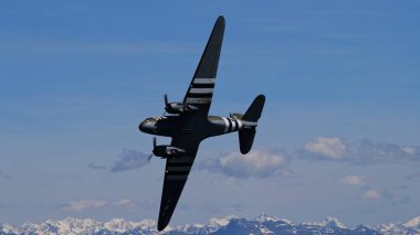 Appenzell İsviçre 30 Mayıs 2025: Klasik askeri uçak açık havada İsviçre Alpleri üzerinde keskin bir şekilde bankacılık yaparken işgal çizgileri sergiliyor. Douglas C-47 Skytrain.