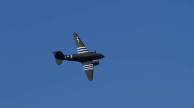 30 Mayıs 2025 Douglas C-47 Skytrain askeri nakliye uçakları mavi gökyüzü arka planında görünen istila çizgileriyle uçuyor. 2. Dünya Savaşı 'ndan kalma savaş kuşu sabit çekimde..