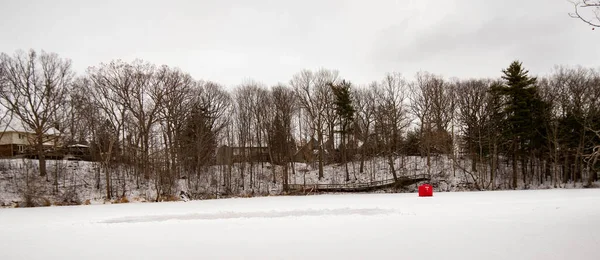 Dorchester, Kanada 'daki donmuş gölette buz pateni pistini temizlemiş. Buz hokeyi sahasında donmuş su üzerinde beyaz kar hareket etti. Donmuş gölde kırmızı buzda balık tutma çadırı
