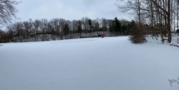 Dorchester, Kanada 'daki donmuş gölette buz pateni pistini temizlemiş. Buz hokeyi sahasında donmuş su üzerinde beyaz kar hareket etti. Donmuş gölde kırmızı buzda balık tutma çadırı