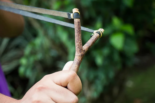 Holding slingshot in hands against green background — Stock Photo, Image