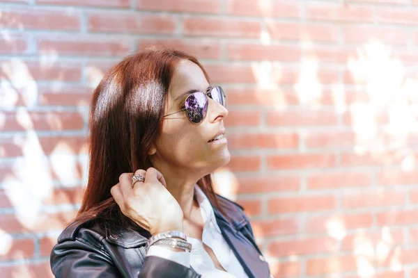 Beautiful woman dressing black jacket, white, shirt and dark sunglasses touching her dark straight hair. Lifestyle. Ring in her hand and bracelets on her wrist. street urban style.