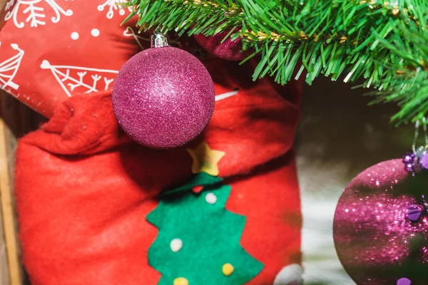 Arka planda bir Noel kutusuyla ağaçta asılı duran mor Noel balosu.