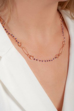 Zarif ve bakımlı, sarı saçlı, beyaz saçlı bir kadının boynuna takılmış renkli bir kolye.