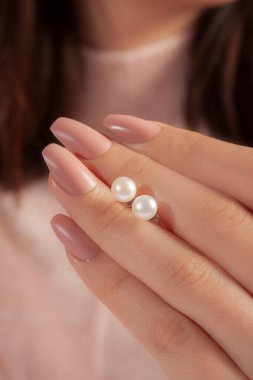 Elleri bakımlı bir kızın elinde bir çift inci küpe.
