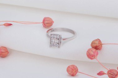 Katmanlı beyaz arka planda pembe çiçekler ve gümüş yüzük