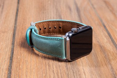 Ahşap zemindeki akıllı saate bağlı mavi deri kayış..