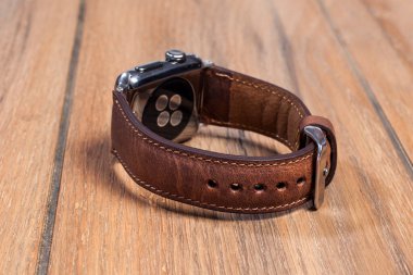 Tahta zemindeki akıllı saate bağlı kahverengi deri kayış..