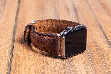 Tahta zemindeki akıllı saate bağlı kahverengi deri kayış..