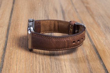 Tahta zemindeki akıllı saate bağlı kahverengi deri kayış..