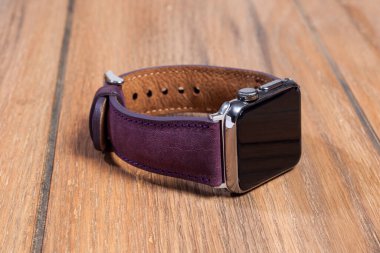 Ahşap zemindeki akıllı saate bağlı mor deri kayış..