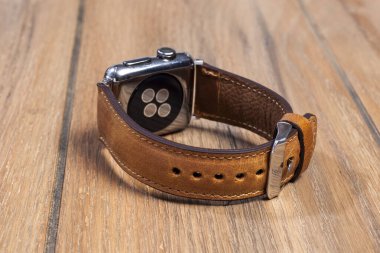 Tahta zemindeki akıllı saate bağlı kahverengi deri kayış..