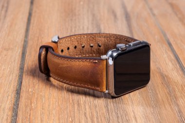 Tahta zemindeki akıllı saate bağlı kahverengi deri kayış..