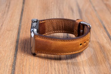 Tahta zemindeki akıllı saate bağlı kahverengi deri kayış..