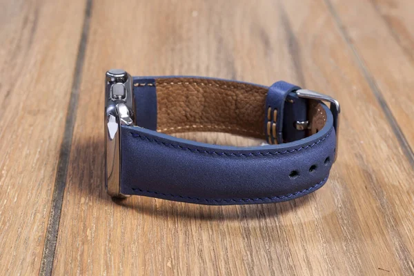 Blue leather strap attached to the smart watch on a wooden floor.