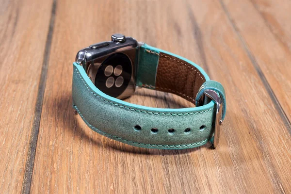 Blue leather strap attached to the smart watch on a wooden floor.